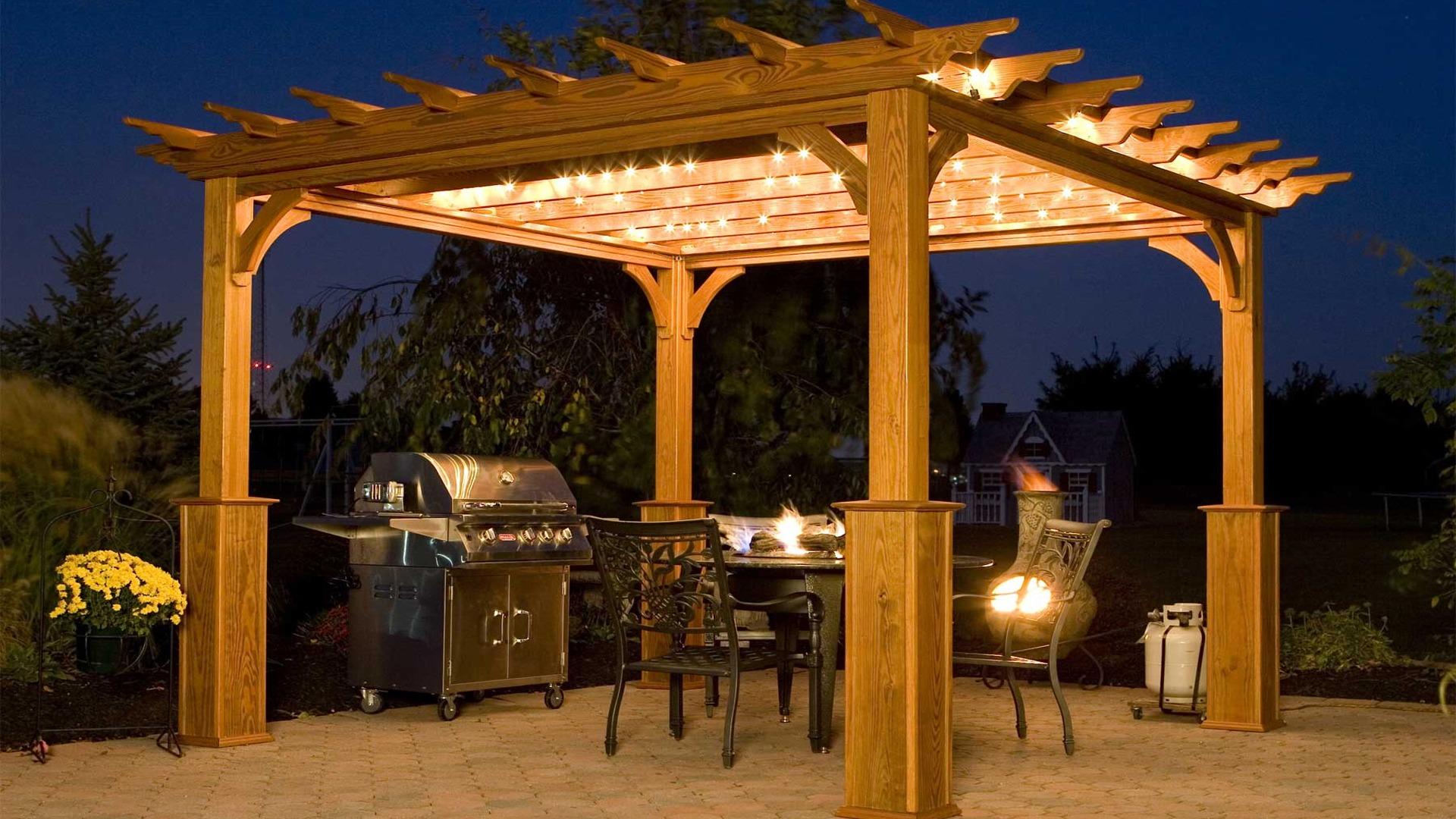 Classic treated timber pergola with string lights and outdoor kitchen BBQ grill at night — warm wood pergola design for Nairobi Kenya